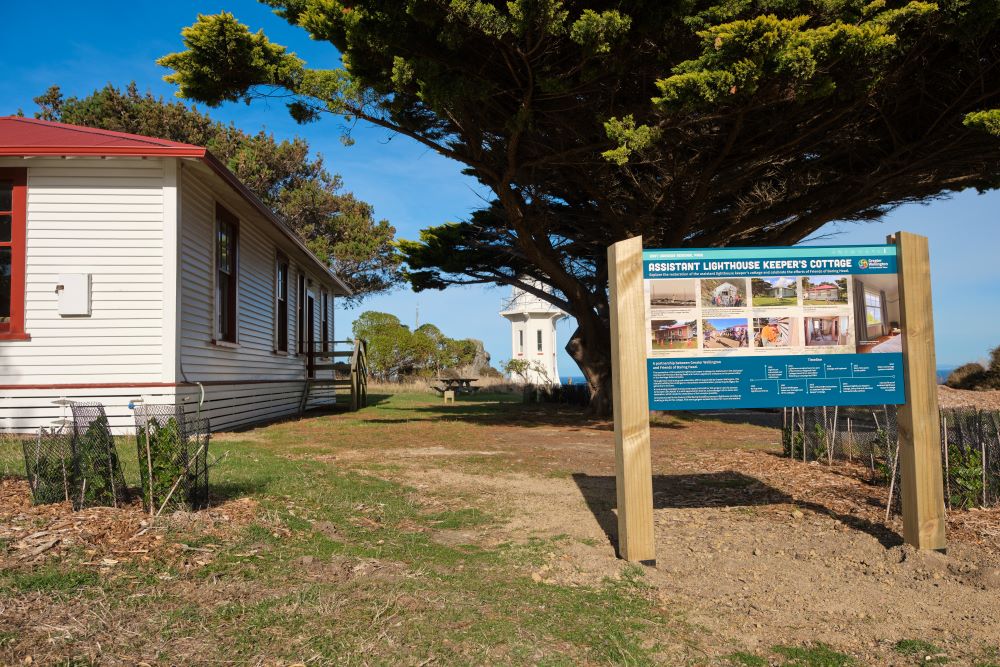 View of the outside of the cottage showing an information sign and the closeness of the lighthouse