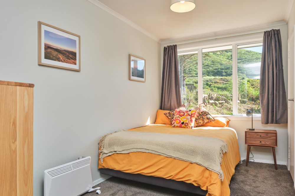 Bedroom three has a queen bed with a yellow duvet, beige footer blanket, and colourful decorative pillows