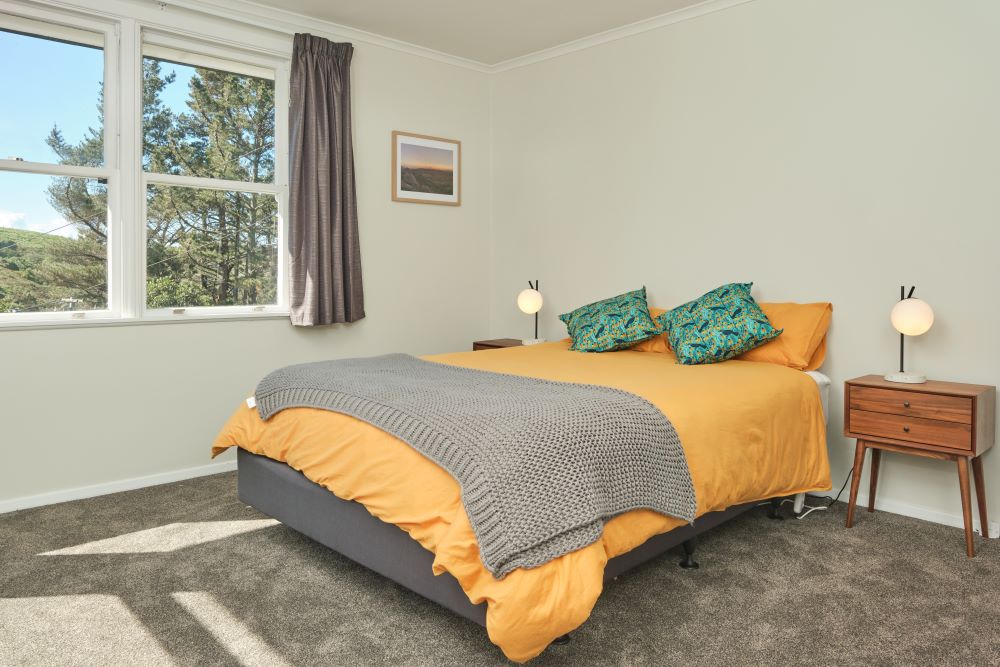 Bedroom one has a queen bed with a yellow duvet, grey footer blanket, and green decorative pillows