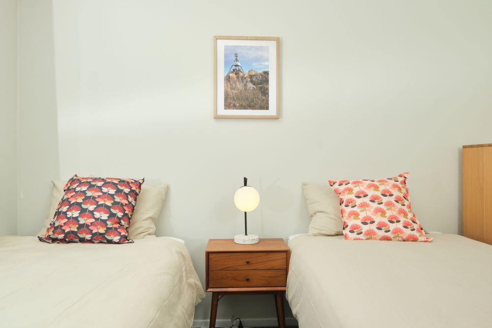 Bedroom two has two single beds separated by a nightstand; the beds both have a beige duvet and a colourful decorative pillow