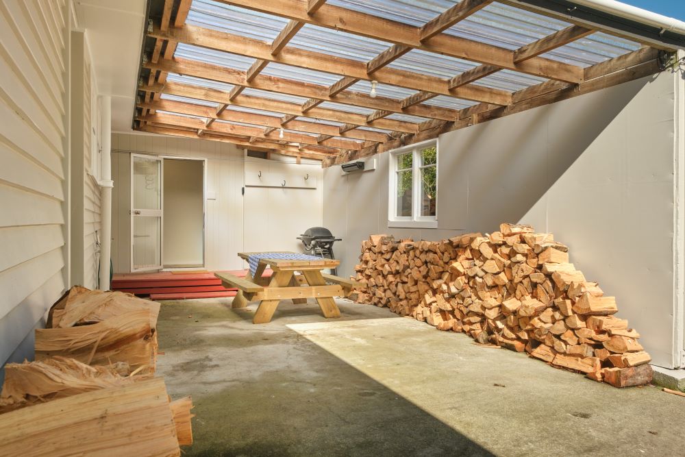 The carport has a picnic table, BBQ, and wood stacked up against two walls