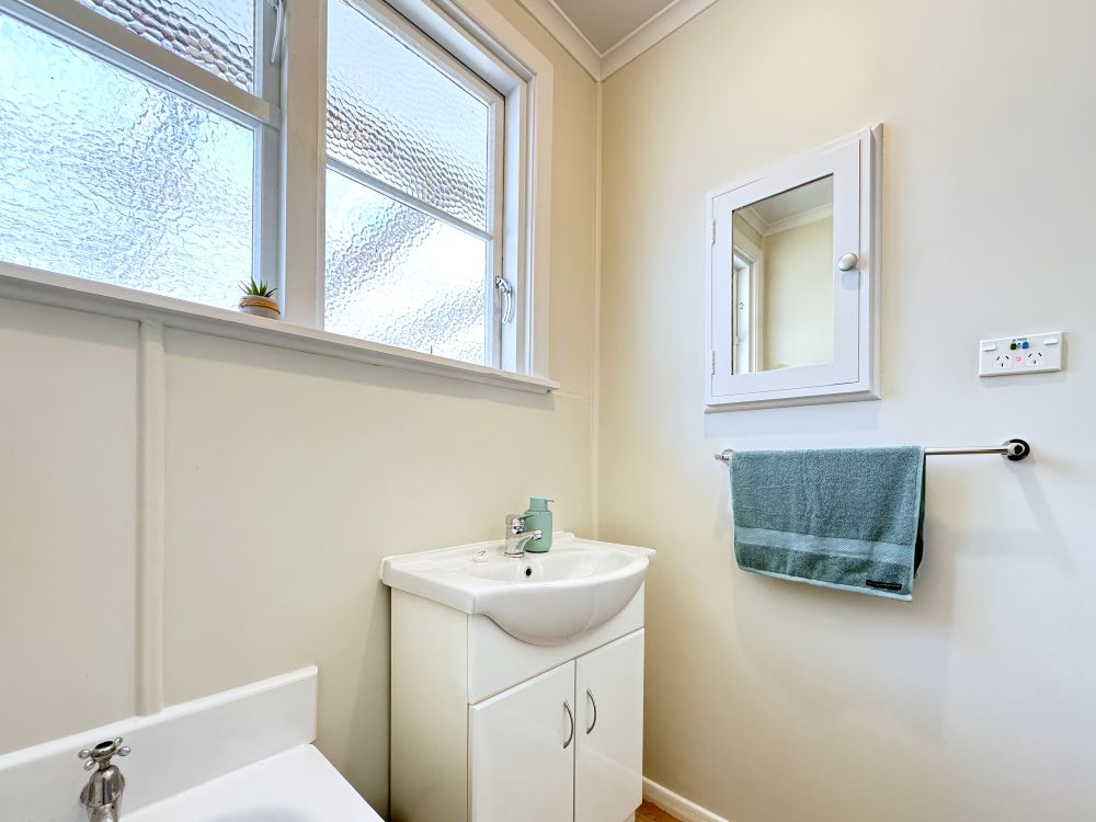 Inside the bathroom, showing the basin, hand towel, medicine cabinet, wall plugs, and privacy windows