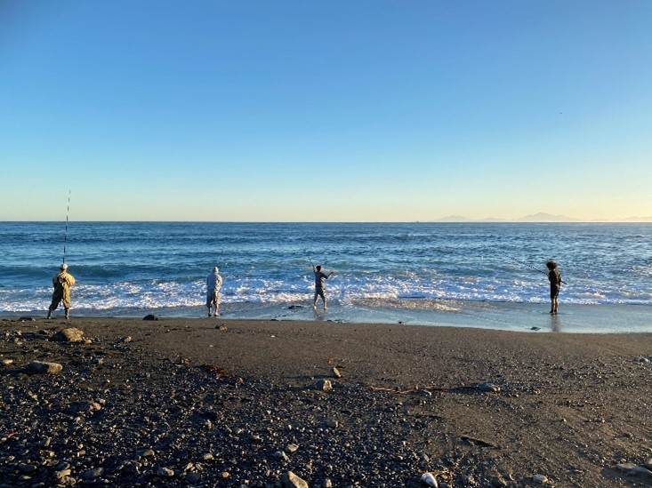 Four people standing on the beach fishing
