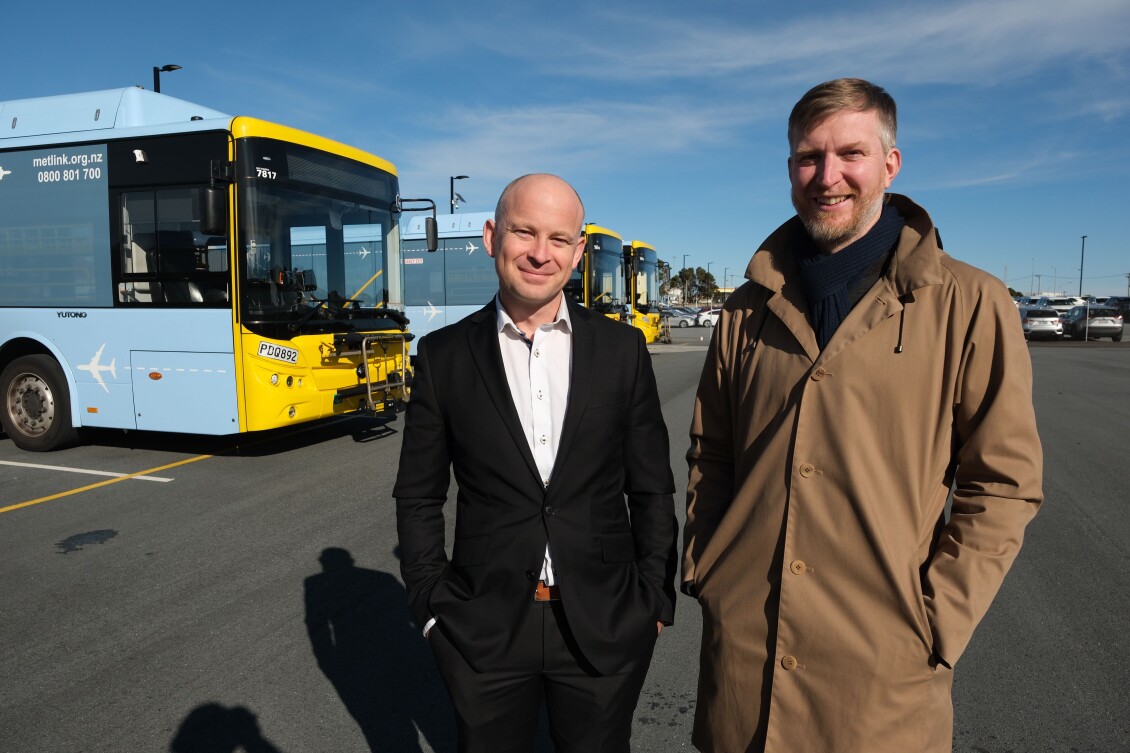 Richard Dalby and Thomas Nash stand in front of an Airport Express bus